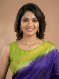 A woman wearing a green and purple tie-dye saree with gold jewelry, posing against a solid beige background.