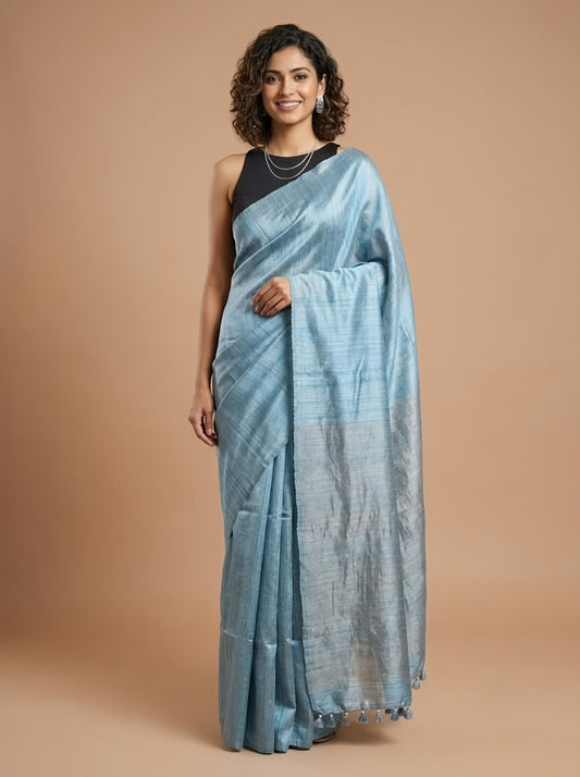 A woman modeling a light blue striped cotton saree with a black sleeveless blouse, standing against a solid beige studio background.