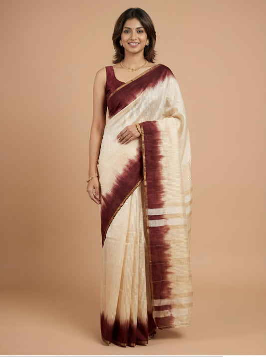 A woman modeling a cream-colored silk saree with a deep maroon tie-dye border and matching blouse, set against a solid beige studio background.