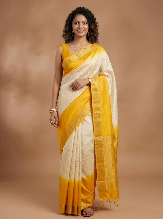 A woman modeling a traditional Indian saree with a yellow and off-white tie-dye pattern, standing against a warm brown studio backdrop.