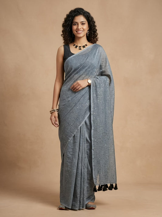 A woman modeling a gray patterned sari with black tassels, paired with a black sleeveless blouse, standing against a solid beige studio backdrop.