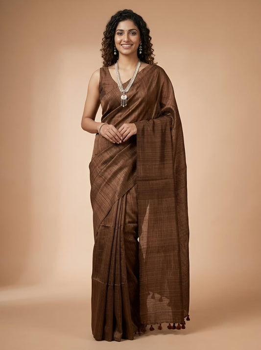 A woman modeling a brown silk saree with a matching sleeveless blouse, standing against a solid beige studio background.