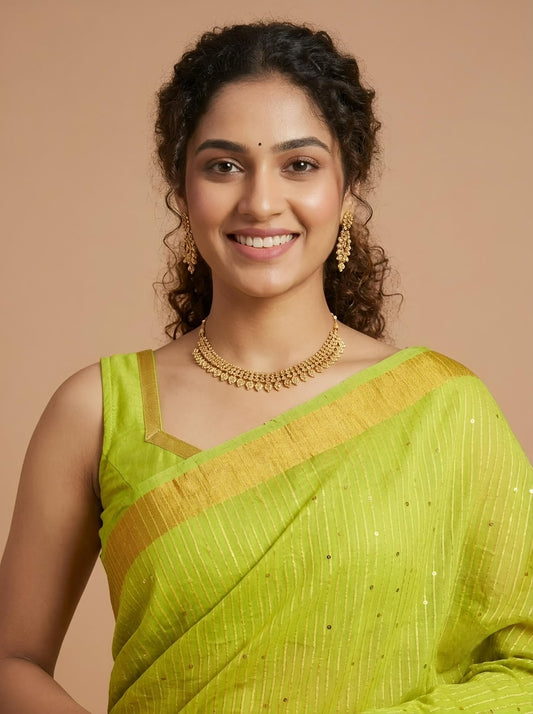 A woman wearing a bright lime green saree with a gold border and gold jewelry, posing against a solid beige background.