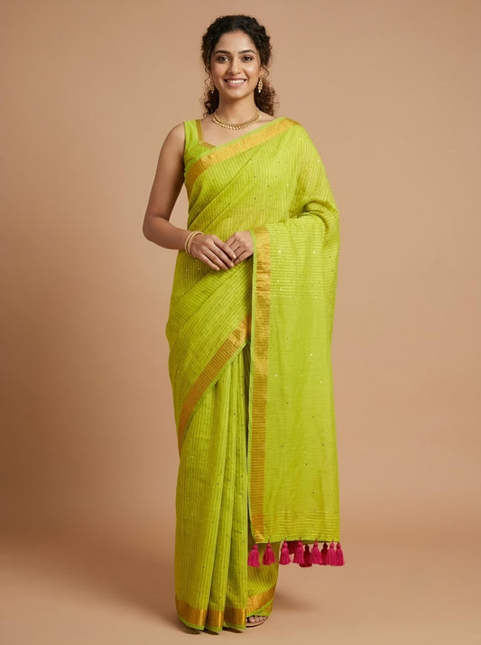 A woman modeling a bright lime green silk saree with gold zari borders and a pink tassel hem, standing against a solid beige studio background.