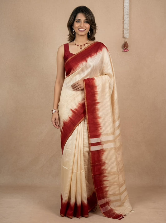A woman modeling a cream-colored silk saree with a deep red tie-dye border and matching red sleeveless blouse, set against a warm beige textured studio backdrop.