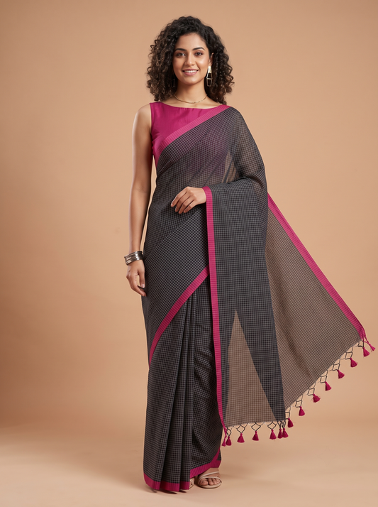 A woman modeling a black and pink checkered saree with a solid pink blouse, standing against a solid beige background.