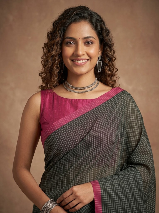 A woman modeling a dark gray and pink saree with a fine grid pattern, featuring a solid pink blouse, set against a warm brown studio background.