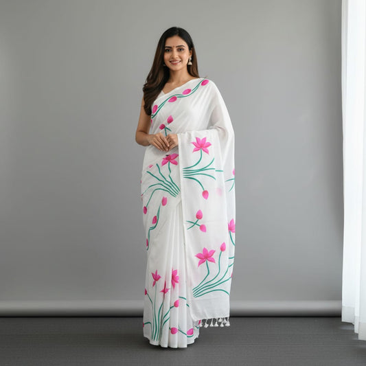 A woman modeling a white saree with a pink and green floral print, standing against a plain gray studio background.