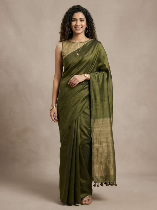 A woman modeling an olive green silk saree with a matching sleeveless blouse against a neutral beige studio backdrop.