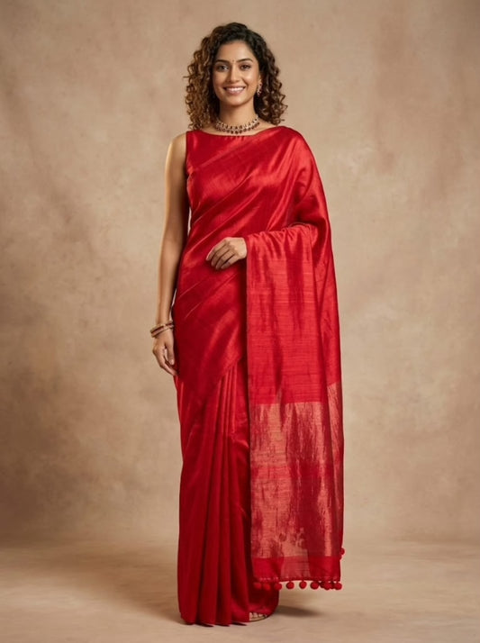 A woman modeling a vibrant red silk saree with a matching red sleeveless blouse, standing against a textured beige studio backdrop.