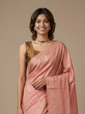 A woman wearing a peach-pink silk saree with gold stripes and a metallic gold blouse, standing against a solid beige background.