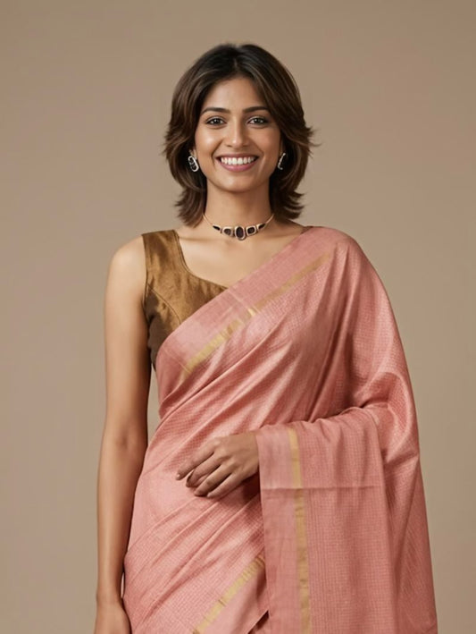 A woman wearing a peach-pink silk saree with gold stripes and a metallic gold blouse, standing against a solid beige background.