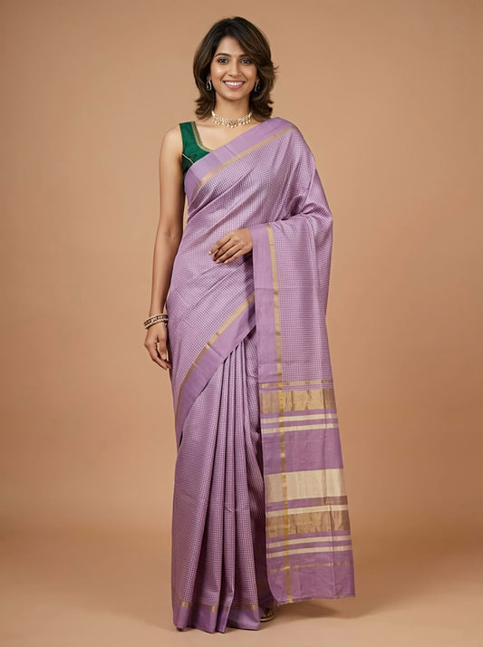 A woman modeling a lavender purple silk saree with gold zari borders and a beige and gold striped pallu, paired with a dark green blouse, against a solid beige studio background.