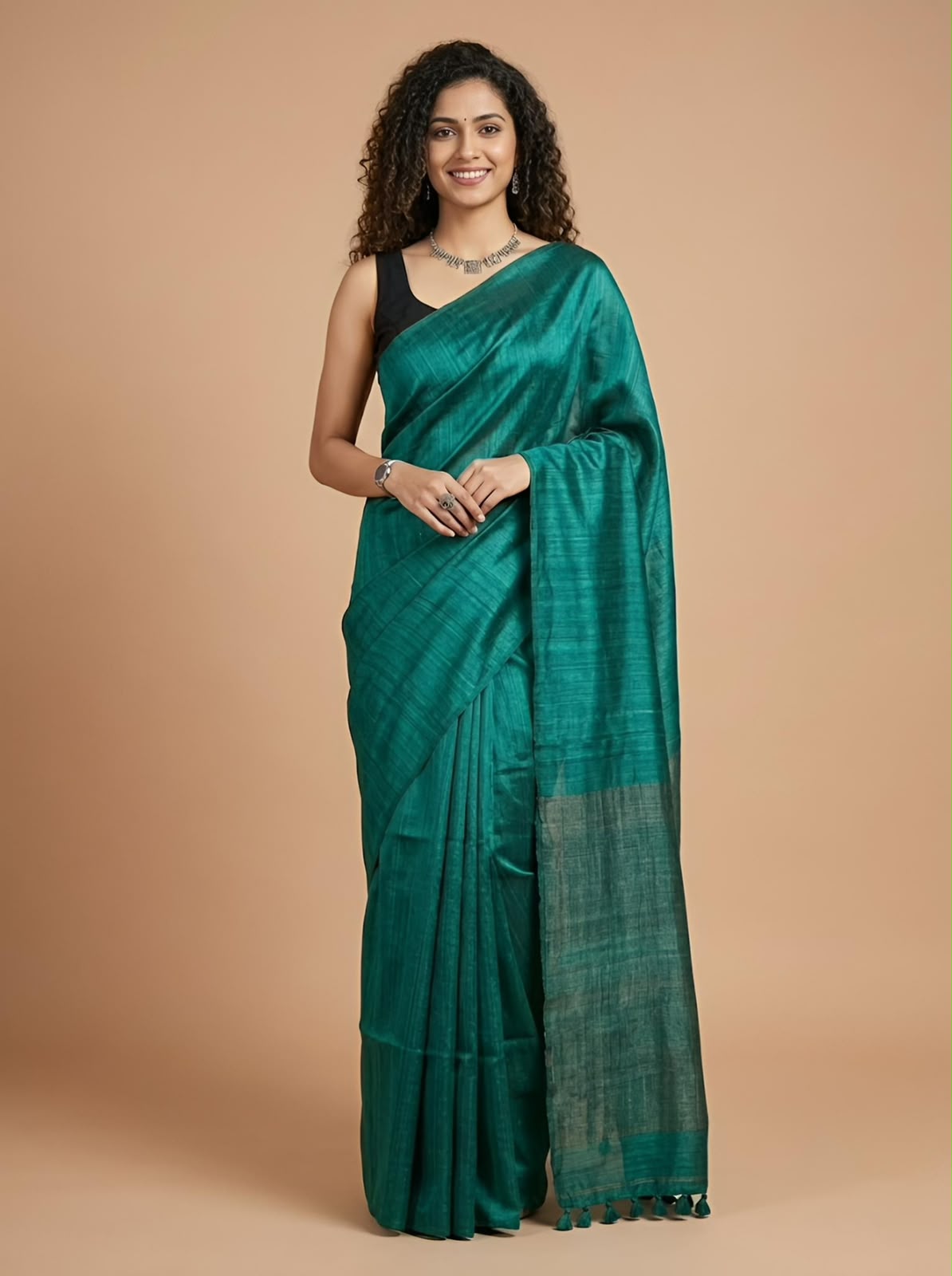A woman modeling a teal green silk saree with a subtle woven pattern and a contrasting black sleeveless blouse, set against a solid warm beige studio background.