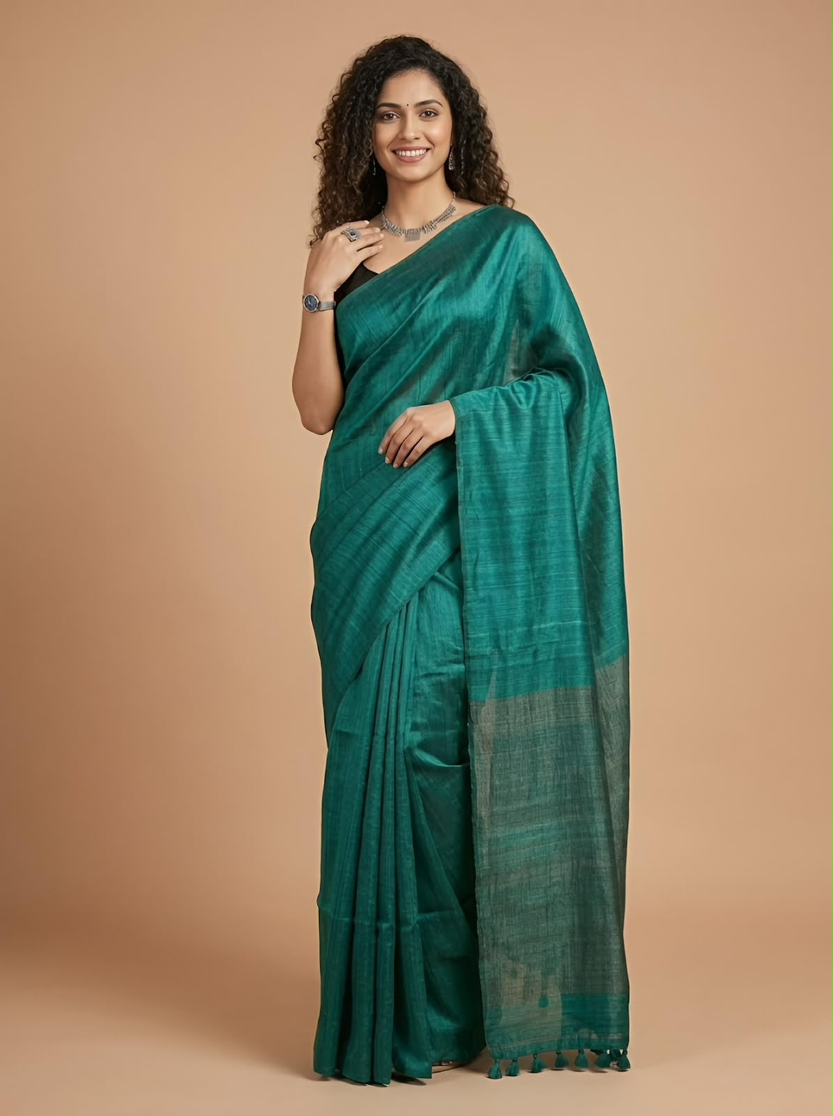 A woman modeling a dark teal green silk saree with a subtle sheen and a contrasting striped border, set against a solid warm beige studio background.