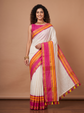A woman models a white silk saree with vibrant pink and orange stripes, paired with a matching pink blouse, set against a solid warm brown studio background.
