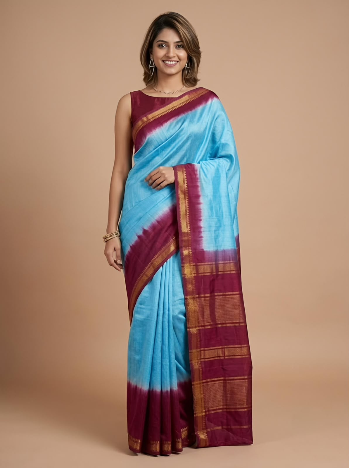 A woman modeling a light blue and deep maroon saree with gold zari stripes, paired with a matching maroon blouse, against a solid beige studio background.
