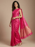 A woman modeling a bright pink silk saree with a matching sleeveless blouse, set against a solid beige studio background.