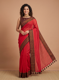 A woman modeling a red silk saree with a brown patterned border and matching blouse against a solid beige studio backdrop.