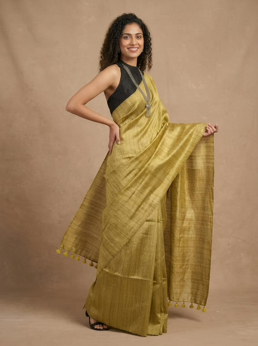 A woman modeling a golden-yellow silk saree with a black sleeveless blouse, standing against a textured beige studio backdrop.