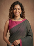 A woman modeling a dark gray and pink saree with a fine grid pattern, featuring a solid pink blouse, set against a warm brown studio background.