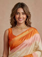 A woman wearing a peach, orange, and cream tie-dye silk saree with a gold zari border, styled with gold jewelry against a solid beige background.